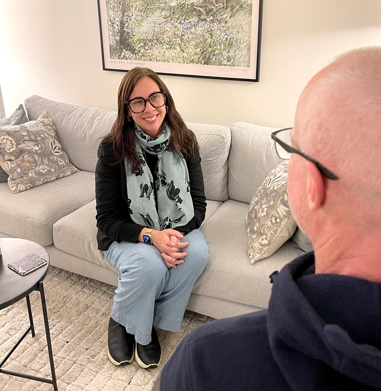 Olive-Counselling-Vancouver-BC-Jane Female therapist with dark hair, smiling, sitting on light grey couch with a male client facing her