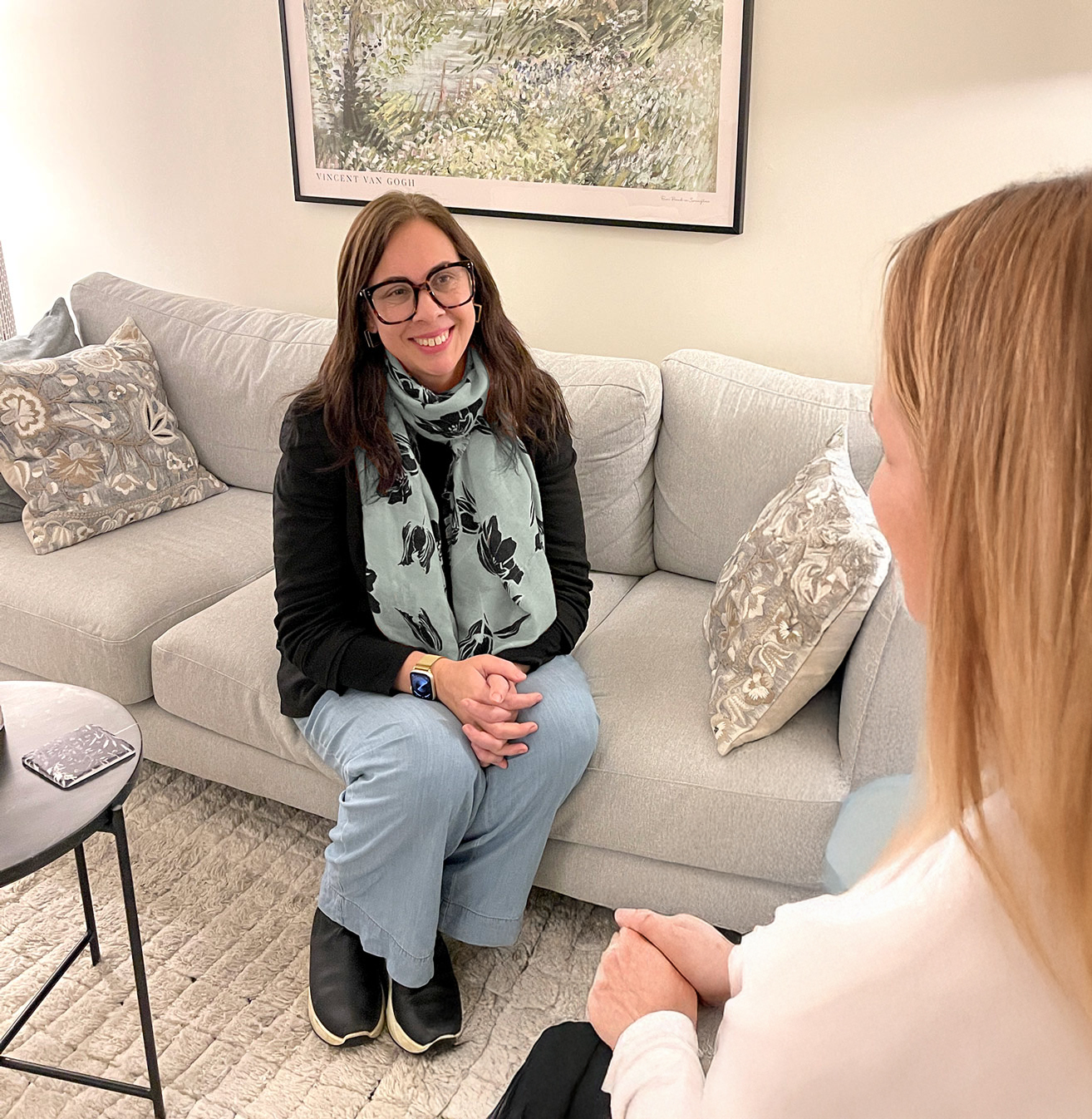 Woman from behind with therapist sitting on couch smiling back at her